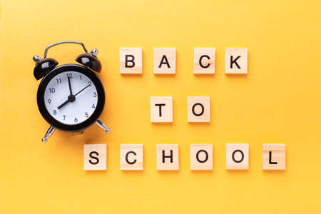 Words Back to school and alarm clock on yellow background. Education, back to school concept, top...