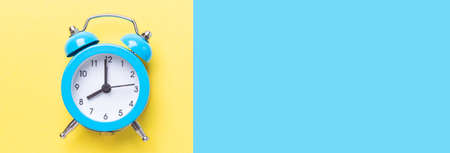Blue alarm clock on two tone color yellow and blue background. Top view, place for text. Long banner...