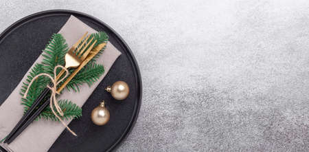 Christmas table setting with black ceramic plate, gifts and fir tree branch on stone background. Top...