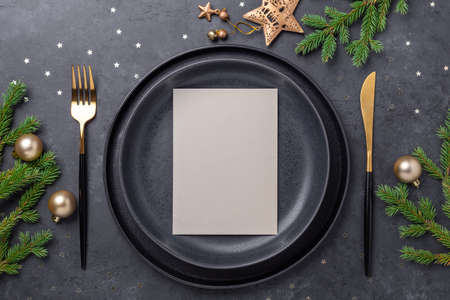 Christmas table setting. Black ceramic plate with blank sheet for your text, fir tree branch and...