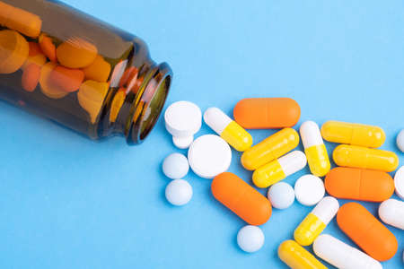 Multicolor tablets and pills capsules from glass bottle on blue background Close-up - Imageの写真素材