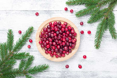 Raw fresh cranberries in wooden bowl and fir branches on light wood background. Top view - Image