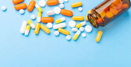 Multicolor tablets and pills capsules from glass bottle on blue background Close-up - Image