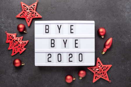 Lightbox with text BYE BYE 2020 with red decoration on dark background. Top view. New year...