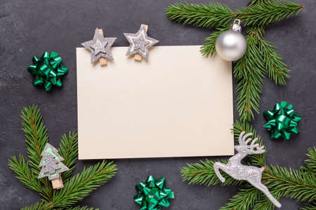 Christmas greeting card with fir tree branch, silver decoration and empty paper mock up. Dark stone...