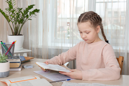 Schoolgirl sitting at desk and reading book. Education Back to school - Image