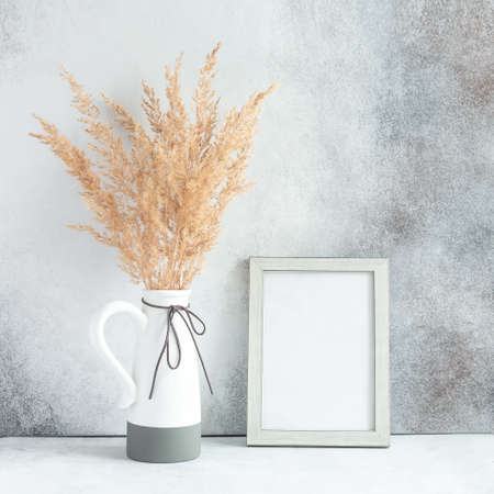 Pampas grass in ceramic vase and empty photo frame against wall. Minimalistic Scandinavian style -...