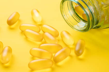 Omega 3 capsules and glass jar on yellow background. Fish oil softgels. Supplement food vitamin D...