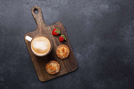 Cup of coffee, cakes and strawberries on a wooden cutting board on dark stone background. Top view. Imageの写真素材