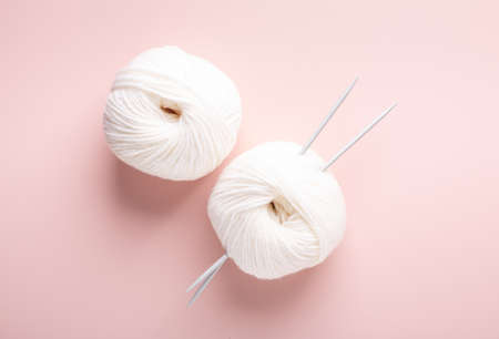 White knitting wool and knitting needles on pastel pink background. Hobby knitting. Top view