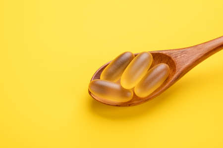 Omega 3 pills in wooden spoon on yellow background. Fish oil softgels. Close up. Copy spaceの写真素材