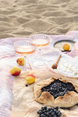Romantic picnic on the beach at sunset. Two glasses of rose, summer fruits, cheese, blueberry galetteの写真素材