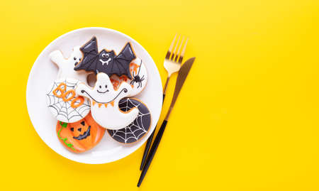 Halloween table setting with gingerbread cookies on white plate and cuterly on yellow background. Bright homemade cookies for Halloween partyの写真素材