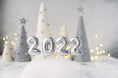 Christmas greeting card with silver number 2022. Yarn wrapped xmas cone trees and garland on backgroundの写真素材