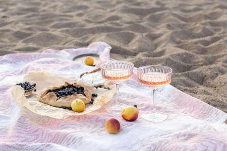 Beautiful summer picnic at sunset on beach with rose wine, cheese, blueberry galette and fresh fruits. Copy spaceの写真素材