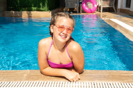 Happy teen girl in pink sunglasses in the swimming pool. Hot sunny vacation conceptの写真素材