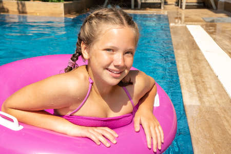 Smiling girl relaxing in swimming pool, floating on pink inflatable ring. Traveling and vacation conceptの写真素材