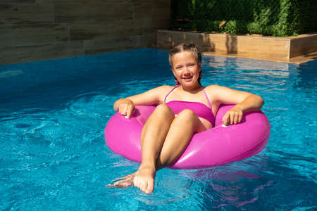 Happy beautiful girl relaxing in swimming pool with turquoise water. Girl floating on pink inflatable ring. Traveling and vacation conceptの写真素材