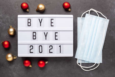 Lightbox with text BYE BYE 2021 with medical mask on dark background. Top view. New year...