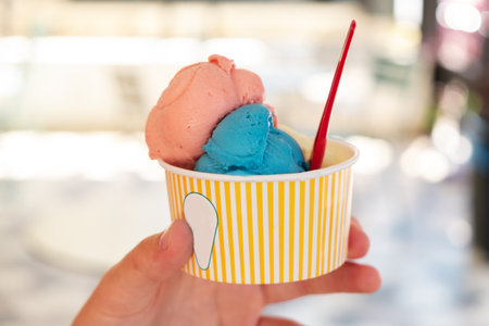 Hand holding paper cup with bright ice cream with different flavors on blurred backgruond Refreshing snack on a hot day Vertical photoの写真素材
