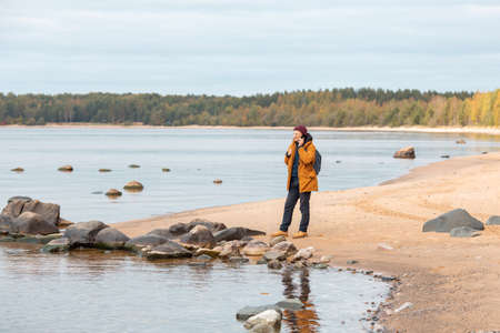 Caucasian man with smartphone in his hand standing in front of lake. A man talking on the phoneの写真素材