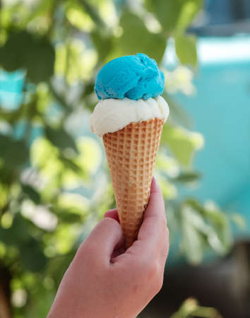Hand holding waffle cone with two ice cream balls on the street Refreshing snack on a hot day Vertical photoの写真素材