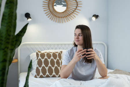Young woman with a cup sitting on a bed. First morning cup of teaの写真素材