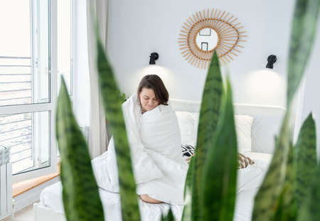 Attractive girl covered with blanket sitting on bed. Young woman enjoying morning on bed at homeの写真素材