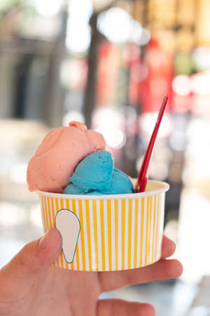 Hand holding paper cup with ice cream on blurred backgruond Refreshing snack on a hot day Vacation concept Vertical photoの写真素材