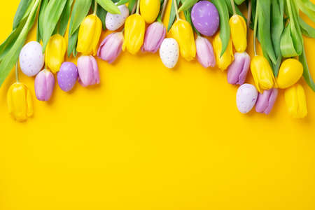 Easter greeting card. Multicolored easter eggs and tulips on yellow background. Easter conceptの写真素材