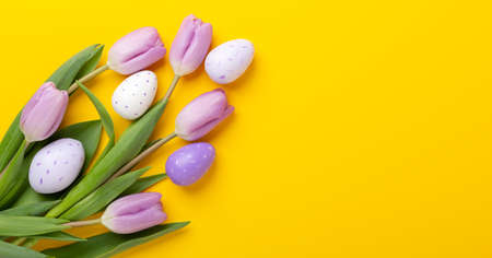 Easter composition. Multicolored easter eggs and tulips on yellow background. Easter concept. Copy...