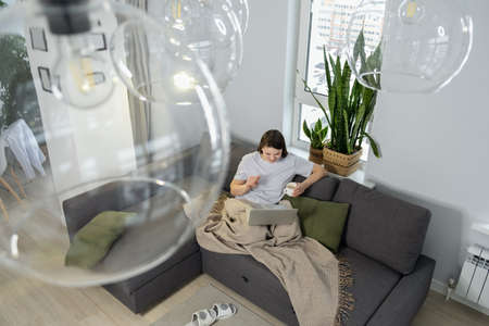Young woman with mug using laptop while sitting on the couch at home. View from above