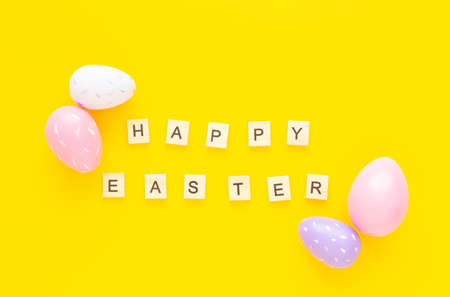 Greeting card with text HAPPY EASTER. Multicolored easter eggs and paper rabbits on yellow backgroundの写真素材