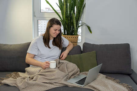 Young woman watching film on laptop while sitting on the couch at homeの写真素材