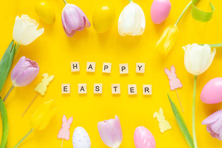 Greeting card with text HAPPY EASTER. Multicolored easter eggs and tulips on yellow backgroundの写真素材
