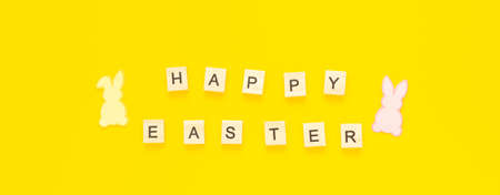 Greeting card with text HAPPY EASTER and paper rabbits on yellow background