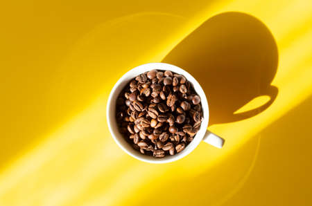 Coffee beans in a white ceramic cup on a yellow background. Hard sun shadows. Top viewの写真素材