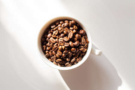 Coffee beans in a white ceramic cup on white background. Hard sun shadows. Top viewの写真素材