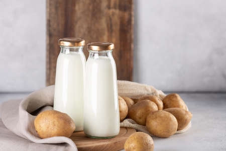 Bottles with vegan plant based milk. Dairy-free drink and potato tubers on gray table - Imageの写真素材