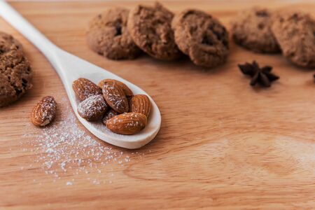 White wooden spoon with almonds, sprinkled with icing sugar on top, against a background of cookies with chocolate and star anise flowers, on a light brown wooden board. Great background for a cafe or restaurant signboard
の写真素材