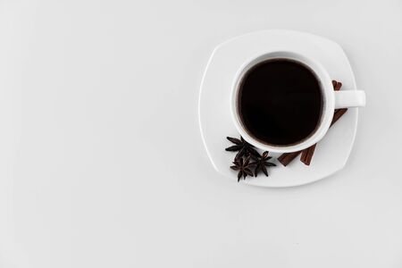 White cup with coffee and saucer, with three star anise star anise and cinnamon sticks, on a white background. A good idea for the menu or sign of a restaurant or cafe, cafeteriaの写真素材