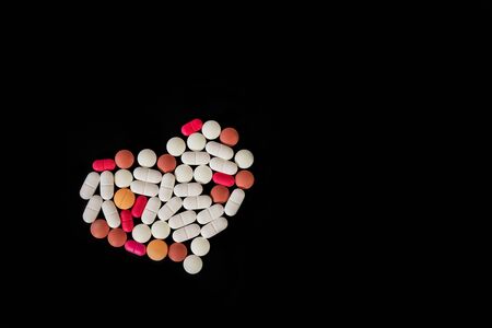 Many different pills and tablets folded in shape of heart on black background. Many pills and...