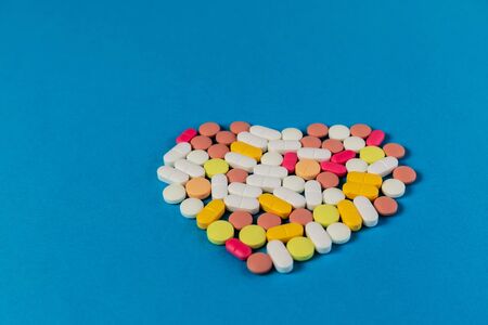 Many different pills and tablets folded in shape of heart on blue background. Many pills and...