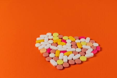 Many different pills and tablets folded in shape of heart on orange background. Many pills and tablets with space for text. Health care. Top view. Copy space. New image. Pharmaceutical pills. Closeupの写真素材