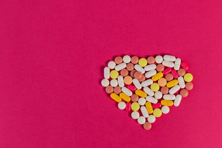 Many different pills and tablets folded in shape of heart on pink background. Many pills and tablets with space for text. Health care. Top view. Copy space. New image. Pharmaceutical pictureの写真素材
