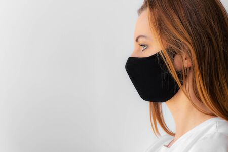 Profile of a young woman in a black medical mask and white t-shirt on a light background. Quarantine of coronavirus epidemic just ended, covid-19. Stay home concept. Virus protection. New realitの写真素材