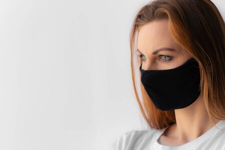 Close-up portrait of a young woman in a black medical mask and white T-shirt on white background. Quarantine, coronavirus epidemic pandemic, covid-19. Stay home concept. Virus protection.の写真素材