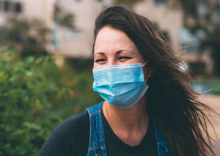 Close-up portrait of young woman in protective medical mask on her face, smiles and squints his eyes...