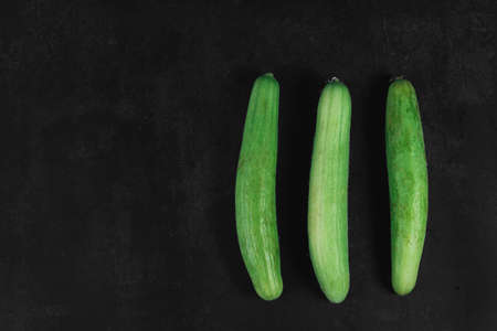 Three organic cucumbers on a dark background. Organic eco food. Healthy diet. Freshly picked vegetables. Fresh greens for salad. Natural organic food. Edible vegetable background. Flat lay, top viewの写真素材