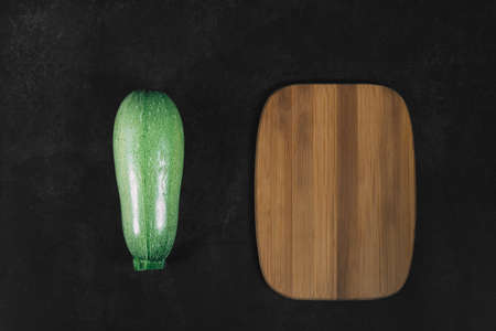 One green squash and wooden brown board on dark background. Organic eco food. Healthy diet. Freshly picked vegetables. Fresh greens for salad. Natural organic food. Edible vegetable background.の写真素材
